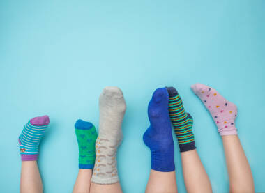 Stopala majke i djece sa čarapama različitih boja na svijetloj plavoj podlozi sa praznim prostotom iznad. Međunarodni Dan osoba sa Down sindromom, 21. mart, podrška i inkluzija, majka i djeca.