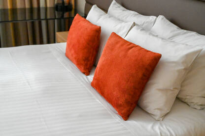 Krevet u hotelskoj sobi. Veliki bijeli i manji crveni, ukrasni jastuci na krevetu.