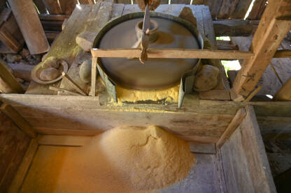 Mlinski kamen se vrti. Kamen melje žito u mlinu. Proizvodnja kukuruznog brašna. Zrna kukuruza padaju u mlin. Tradicionalna vodenica na rijeci.