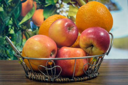 Narandže i jabuke u korpi na stolu u pozadini plodovi na granama