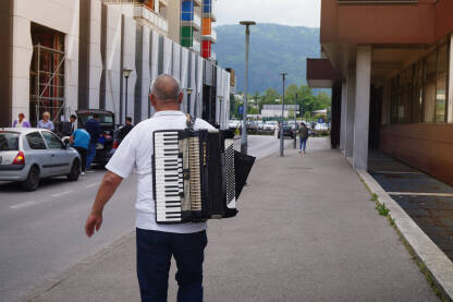Harmonikaš na ulici Čovjek hoda ulicom sa harmonikom na leđuma.