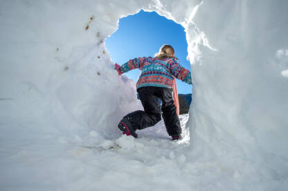 Djevojčica izlazi iz snježne kućice. Igranje u snijegu tokom raspusta. Dječije zimske radosti.