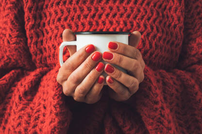 Ženske ruke drže metlanu šolju uz crveni pleteni džemper.