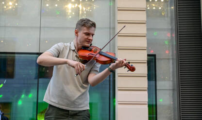Čovjek svira violinu na gradskom trgu. Ulični svirač svira violinu. Violinista zabavlja publiku na javnom trgu. Ulični nastup.