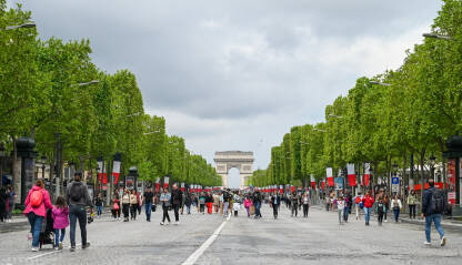 Pariz, Francuska: Turisti šetaju čuvenom avenijom Champs-Élysées u Parizu, s Trijumfalnom kapijom u pozadini. Ljudi šetaju ulicom u blizini poznatih znamenitosti.