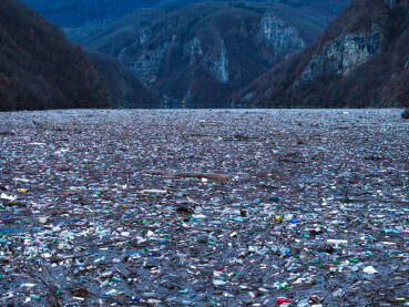 Razni oblici komunalnog otpada nagomilani u rijeci Drini, vidljivi na površini i uz obalu.