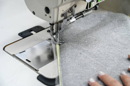 Žena šije tekstil šivaćom mašinom. Radnica radi u fabrici. Krupni plan djevojčinih ruku dok šije tkaninu u fabrici.