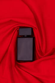 Crna bočica parfema umotana u crvenu tkaninu kao pozadina