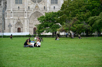 Mladi se druže na travi u parku u Beču, Austrija. Ljudi sjede na zelenoj travi u parku.