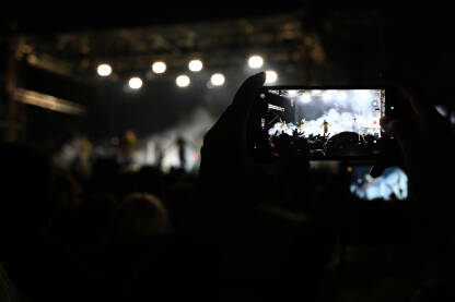 Djevojka mobitelom snima nastup benda na koncertu. Djevojka sa mobitelom snima nastup benda na koncertu. Snimanje muzičara na bini tokom festivala.