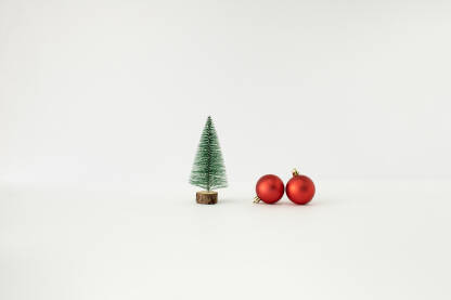 Božićno drvce i dvije crvene ukrasne kuglice na bijeloj pozadini.