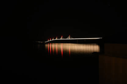 Osvijetljeni most preko mora noću. Veliki bijeli viseći most iznad vode. Pelješki most, Hrvatska.