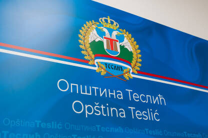 Grb Opštine Teslić na plavoj pozadini sa latiničnim,ćiriličnim i engleskim natpisom Opština Teslić. Krupni kadar.