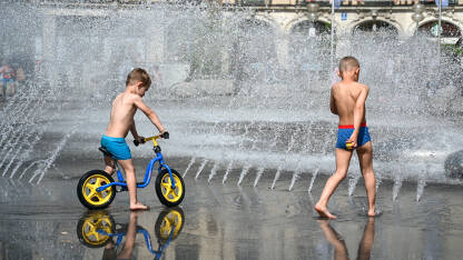 Dječaci se osvježavaju na fontani. Djeca se osvježavaju pod vodom tokom vrelog ljetnog dana. Toplotni talas u gradu.
