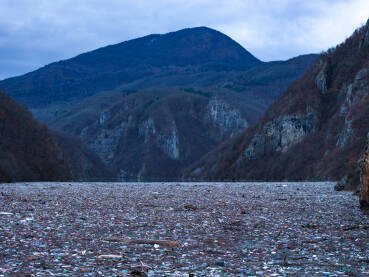 Razni oblici komunalnog otpada nagomilani u rijeci Drini, vidljivi na površini i uz obalu.