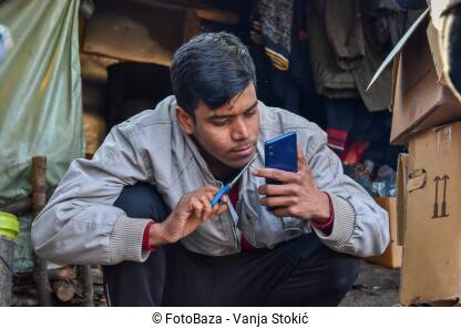 Migrant uređuje bradu makazama. Izbjeglica se ogleda na telefonu i makazama skraćuje bradu.