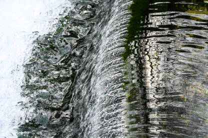 Riječni tok u proljeće, duga ekspozicija. Kristalno čista voda koja teče preko stijena i zelene mahovine. Voda polako teče po kamenju blizu izvora. Mali slap u prirodi.
