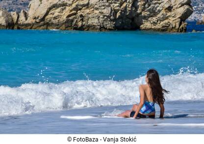 Djevojka sjedi sama na plaži u Ksamilu, Albanija. Uživanje u morskim talasima. Djevojčica sjedi na obali mora.