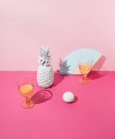 Tropska ružičasta pozadina s bijelim ananasom, limunom, čašama za piće i lepezom od plavog papira. Minimalni koncept.