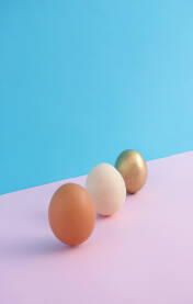 Tri jajeta različitih boja u prostoru na pastelnoj pink, roze i svijetloplavoj podlozi.