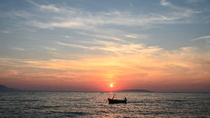 Silueta ribarskog broda tokom zalaska sunca. Brodica na moru.