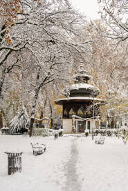 Muzički paviljon u parku At Mejdan,  okružen svježim snijegom, zimskim granama i tihom atmosferom grada. Utabana staza vodi prema paviljonu.