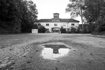 Ulazna kapija nacističkog koncentracionog logora Dachau, Njemačka. Ulazna kapija nacističkog koncentracionog logora Dachau, Njemačka. Memorijalni centar logora Dachau, crno bijela fotografija. Kapija logora sa natpisom "Arbeit macht frei" (prijevod: rad oslobađa).