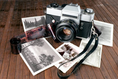Analogni fotoaparat sa fotografijama i filmom Analogni stari foto aparat na stolu sa razbacanim crno-bijelim fotografijama i filmom