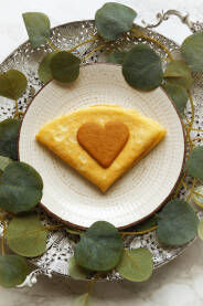 Palačinak na tanjiru sa biskvitom u obliku srca i dekoracijom od lišća.