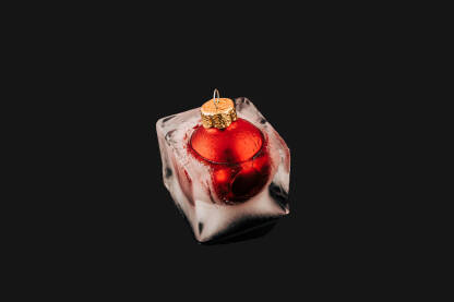 Crvena božićna kuglica / ukras zaleđena u kocki leda. Božićna, Novogodišnja čestitka.
