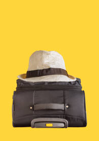Slamnati šešir na putnom koferu crne boje sa žutom pozadinom. Putovanje, godišnji odmor - koncept sa praznim prostorom, copy space, za pisanje, reklamu, obradu.