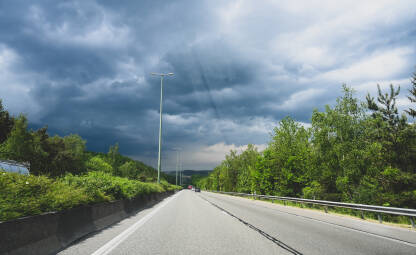 Vožnja autocestom po olujnom vremenu. Pogled vozača na asfaltnu cestu sa sivim oblacima u daljini.