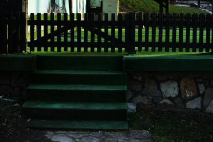 Ogradica od drveta i zeleni tepih koji je na stepenicama i bini, dekorativni kamen