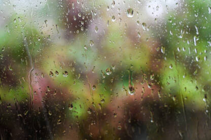 Kapljice vode na prozorskom staklu. Kapi kiše na staklu automobila i zelena šuma u pozadini. Kišni dan u proljeće.