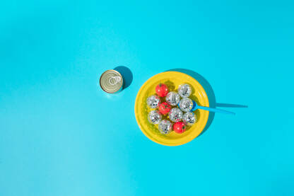 Žuti plastični tanjur s cherry rajčicama, disko kuglama, plavom plastičnom kašikom i konzervom.