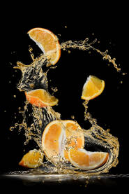 Isječena narandža na kriške poprskana vodom na crnoj pozadini. Komadići narandže plutaju u zraku.