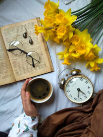 Šolja kafe uz predivne žute narcise. Na slici su i starinski budilnik, kao i naočare i minđuše.
