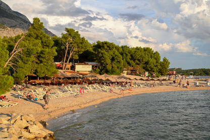 Makarska, Hrvatska. Ljudi uživaju na plaži uz more. Turisti na pješčanoj plaži tokom zalaska sunca. Godišnji odmor.
