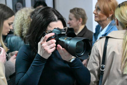 Mlada fotoreporterka fotografiše ljude na javnom događaju. Fotografkinja prati javni događaj profesionalnom kamerom. Novinarka fotografiše ljude.