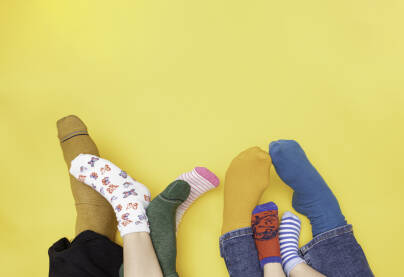 Stopala porodice na žutoj podlozi sa  čarapama različitih boja kao simbol podrške osobama sa Down sindromom. 21. mart - Međunarodni dan osoba sa Down sindromom. Otac, majka, kćerka i sin.