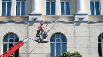 Radnik pere fasadu i prozore na zgradi.