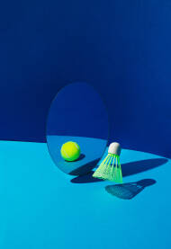 Loptica za badminton s refleksijom teniske loptice u ogledalu na plavoj pozadini.
