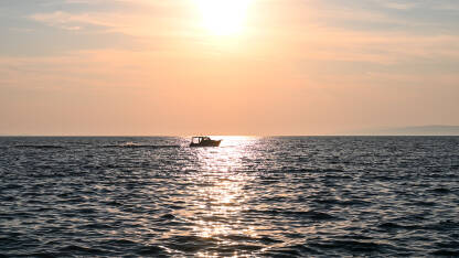 Silueta čamca na zalasku sunca. Brodica na moru. Ribarski brod plovi po dubokom plavom moru.