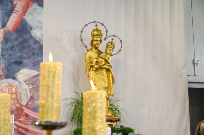 Zapaljene svijeće u crkvi. Kip Djevice Marije i Isusa Krista u pozadini. Ukrašen oltar za Božić.