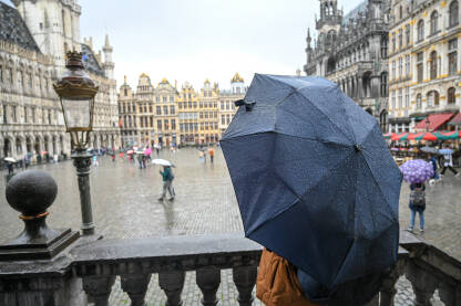 Žena drži kišobran dok pada kiša. Ljudi na trgu u centru grada po kišnom danu.