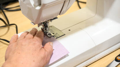 Žena šije tkaninu šivaćom mašinom. Žena radi u fabrici. Krojačica.