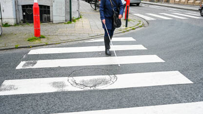 Slijepa osoba prelazi ulicu uz pomoć štapa. Slijepa žena hoda po ulici koristeći bijeli štap.