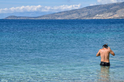 Muškarac se sprema za ronjenje u moru. Mladić stoji u vodi i stavlja masku za ronjenje.