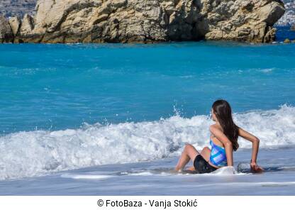 Djevojka sjedi sama na plaži u Ksamilu, Albanija. Uživanje u morskim talasima. Djevojčica sjedi na obali mora.
