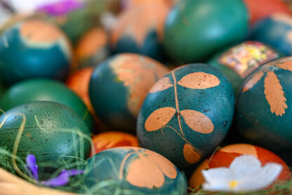 Jaja plave boje, ukrašena šarom biljke, spremna za pravoslavni praznik Vaskrs.  Korpa puna ofarbanih jaja, crvene i plave boje.